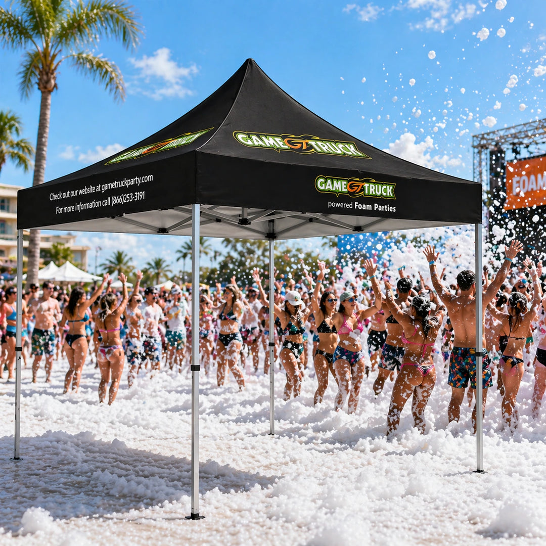 Black tent with 'Game Truck' branding at a beach party with people in swimwear and foam.